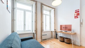 A room with a sofa, a desk with a computer, a TV, and a window with a view.