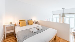 A bedroom with a large bed, two bedside tables, a nightstand, a window with curtains, and a hanging light fixture.