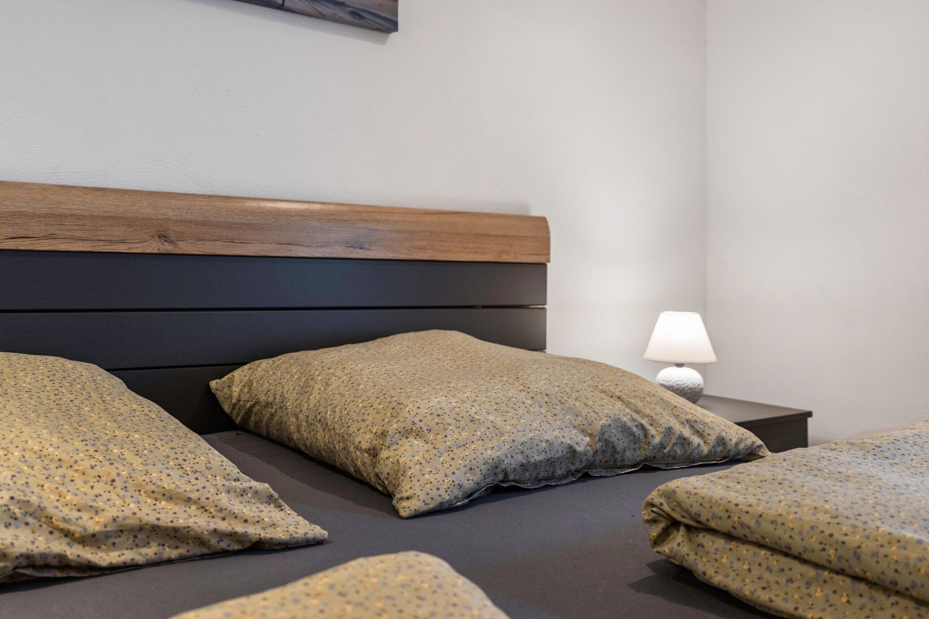 Una cama con cabecera de madera, dos almohadas y una lámpara de noche.