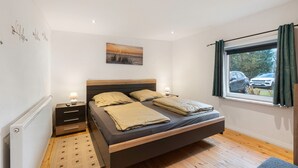 A bedroom with a bed, bedside tables, a window with curtains, a radiator, and a wall art piece.