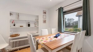 A dining area with a wooden table, white chairs, a radiator, and a window with curtains.
