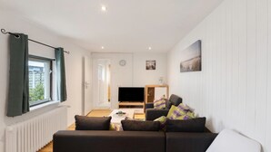 A living room with a sofa, a coffee table, a TV, and a window with curtains.