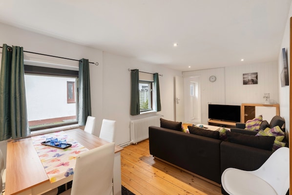 A modern living room with a sofa, a TV, and a dining area with a table and chairs.