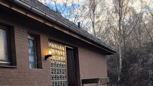 Edifici de maó amb una escala que porta a una porta, una finestra amb un llum i vistes a arbres i un terra cobert de neu.