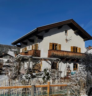 Un edificio a due piani con balconi in legno, facciata bianca e paesaggio innevato.