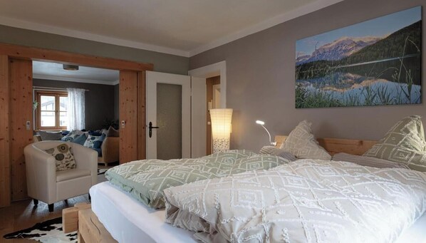 A bedroom with two beds, a chair, a lamp, and a painting of a mountain landscape. - Apartment 'Bienennest' with Mountain View, Balcony and Wi-Fi (Mittenwald)