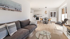 A modern living room with a sofa, a glass coffee table, and a dining area with chairs and a table. - Apartment 'Ferienhaus Waterkant Mit Hund' with Private Terrace, Private Garden and Wi-Fi (Klanxbüll)