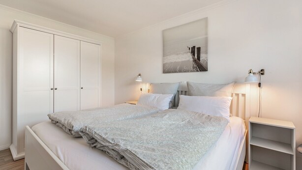 A bedroom with a bed, two bedside tables, a nightstand, a wardrobe, and a wall-mounted artwork. - Apartment 'Ferienhaus Waterkant Mit Hund' with Private Terrace, Private Garden and Wi-Fi (Klanxbüll)