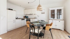A modern kitchen with white cabinets, a dining table with chairs, a hanging light fixture, and a cabinet with glass doors. - Apartment 'Ferienhaus Waterkant Mit Hund' with Private Terrace, Private Garden and Wi-Fi (Klanxbüll)