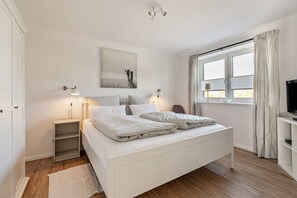 Une chambre à coucher comprenant un lit, des tables de chevet, un meuble pour la télévision, une fenêtre avec des rideaux et un tableau accroché au mur.
