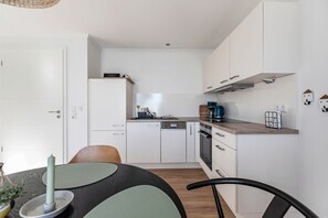 Une cuisine moderne avec des meubles blancs, un plan de travail en bois et un coin repas comprenant une table et des chaises.