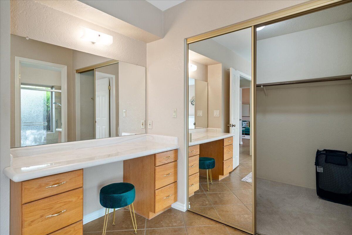 A modern bathroom with a large mirror, wooden cabinets, and teal stools.