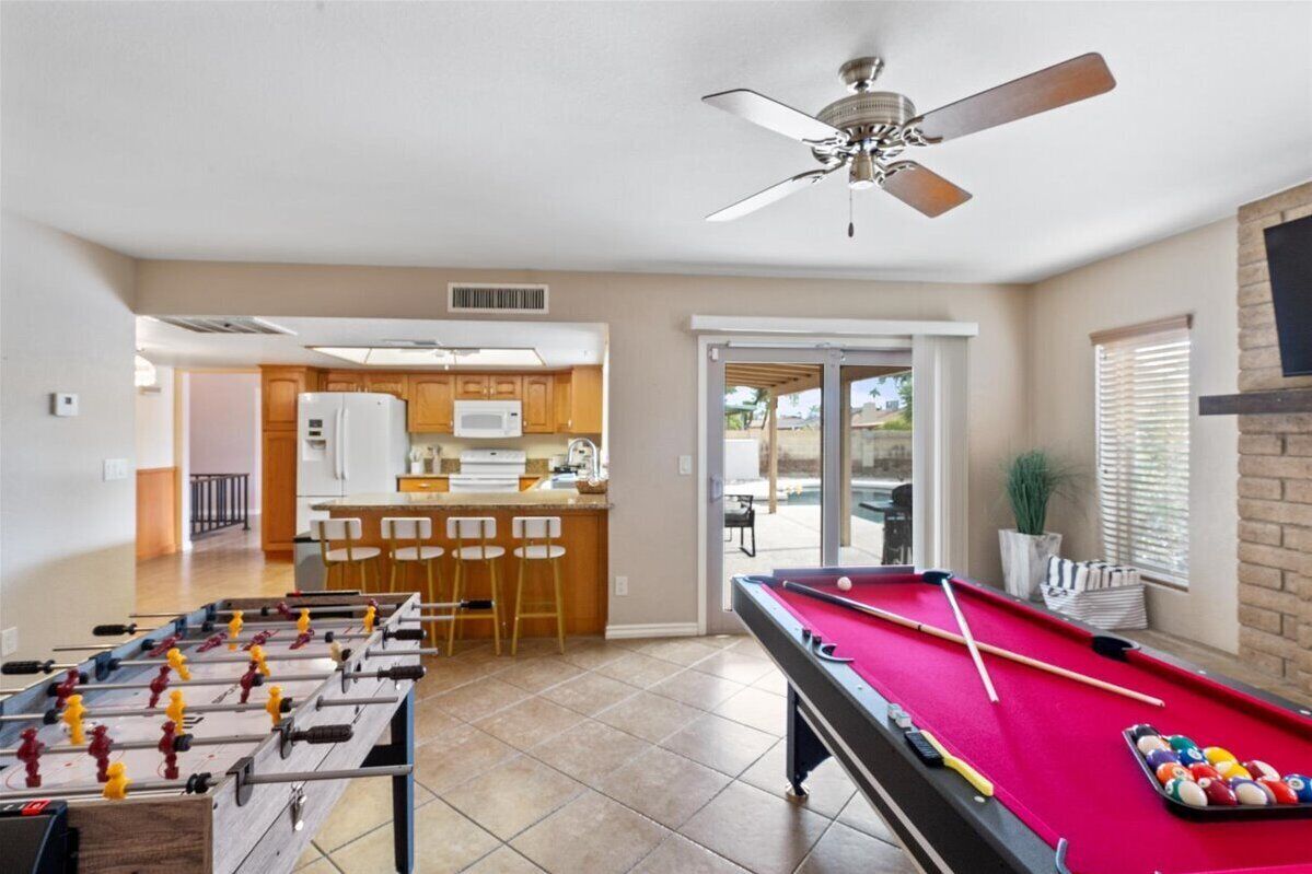 Un vaste espace de vie comprenant une table de baby-foot, une table de billard et un ventilateur de plafond.