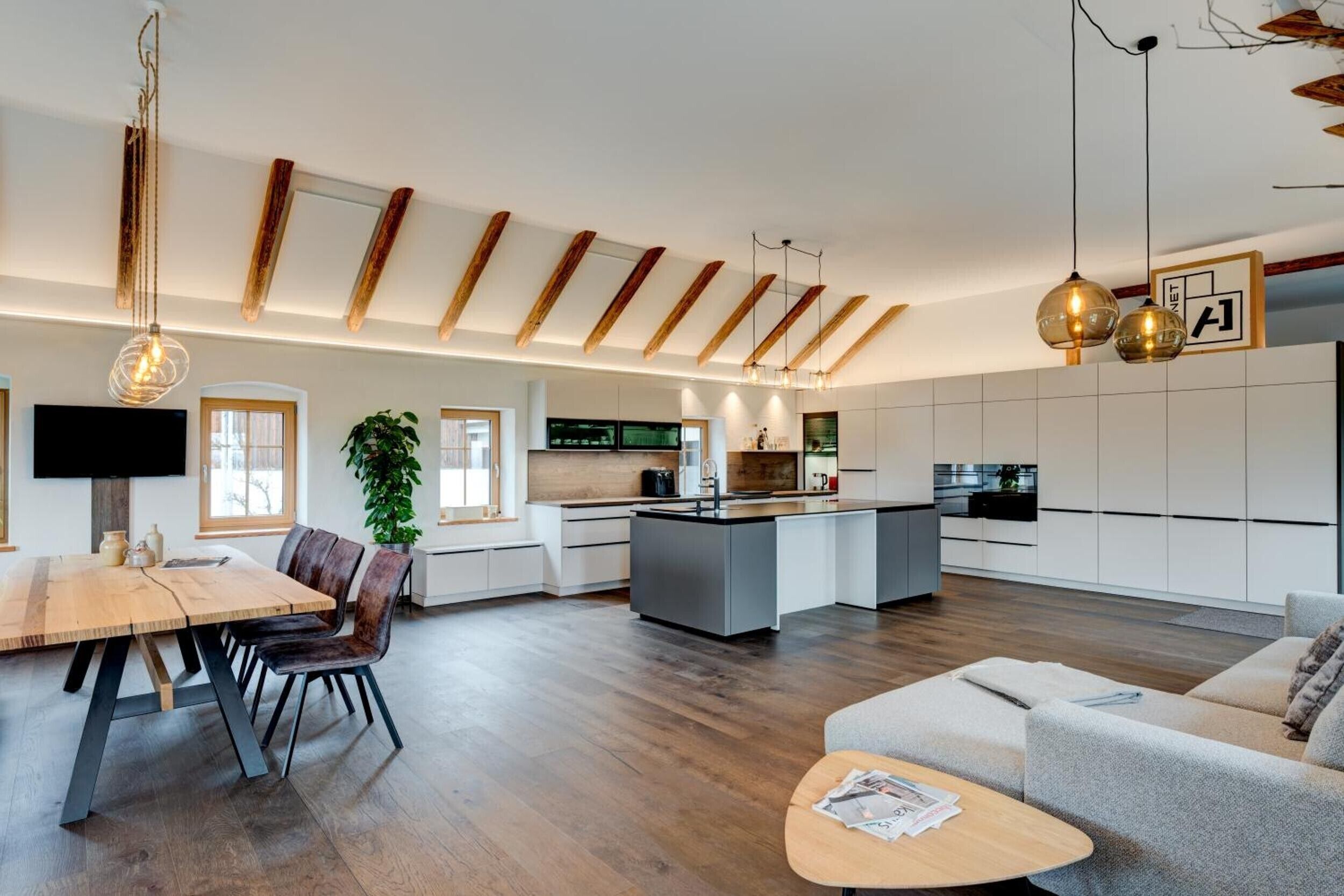 A modern kitchen with a central island, wooden beams on the ceiling, and pendant lighting.