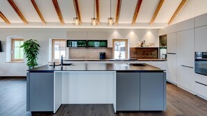 A modern kitchen with a central island, wooden beams, pendant lighting, and built-in appliances. - Studio Apartment 'Außergewöhnliches Loft' with Mountain View and Wi-Fi (Senftenbach)