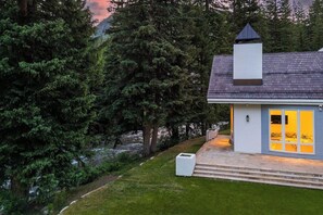 A modern house with a stone staircase leading to a porch, surrounded by dense trees. - 6 Bedroom Riverside Haven in East Vail (Vail)