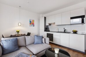 A modern kitchen with white cabinets, a Bosch microwave, and a dining area with a gray sofa and blue pillows.
