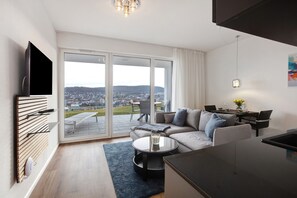 A modern living room with a sofa, coffee table, and dining area, featuring a large sliding glass door to a balcony with a city view. - Apartment 'Panoramablick' with Mountain View, Private Terrace and Wi-Fi (Lörrach)