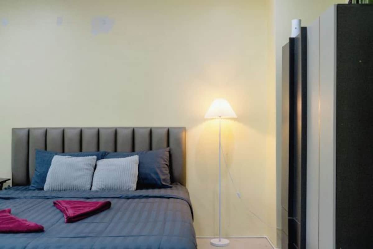 A bedroom with a bed, pillows, a floor lamp, and a wardrobe.
