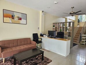 Uma sala de estar moderna com um sofá marrom, uma cadeira de escritório preta, uma escrivaninha de madeira com um computador e um ventilador de teto.