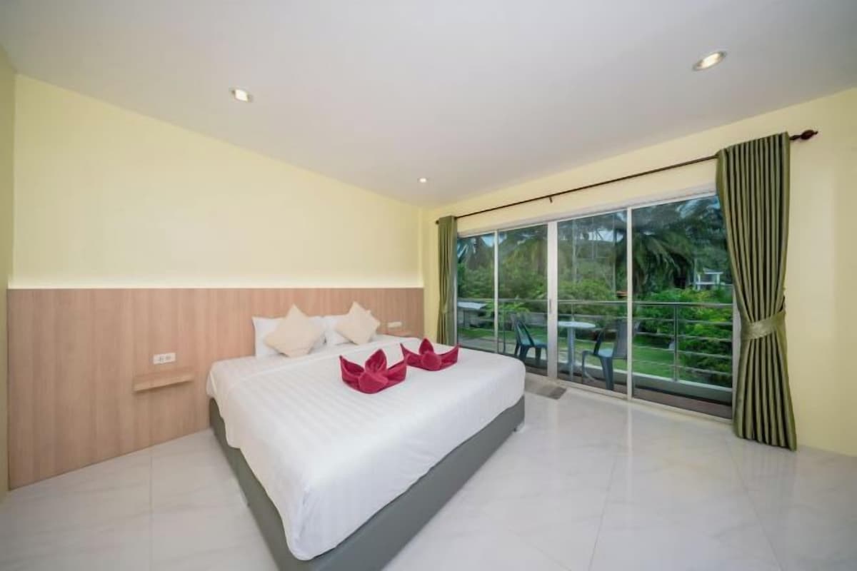 A hotel room with a large bed, a wooden headboard, a small bedside table, and a large sliding glass door leading to an outdoor area.
