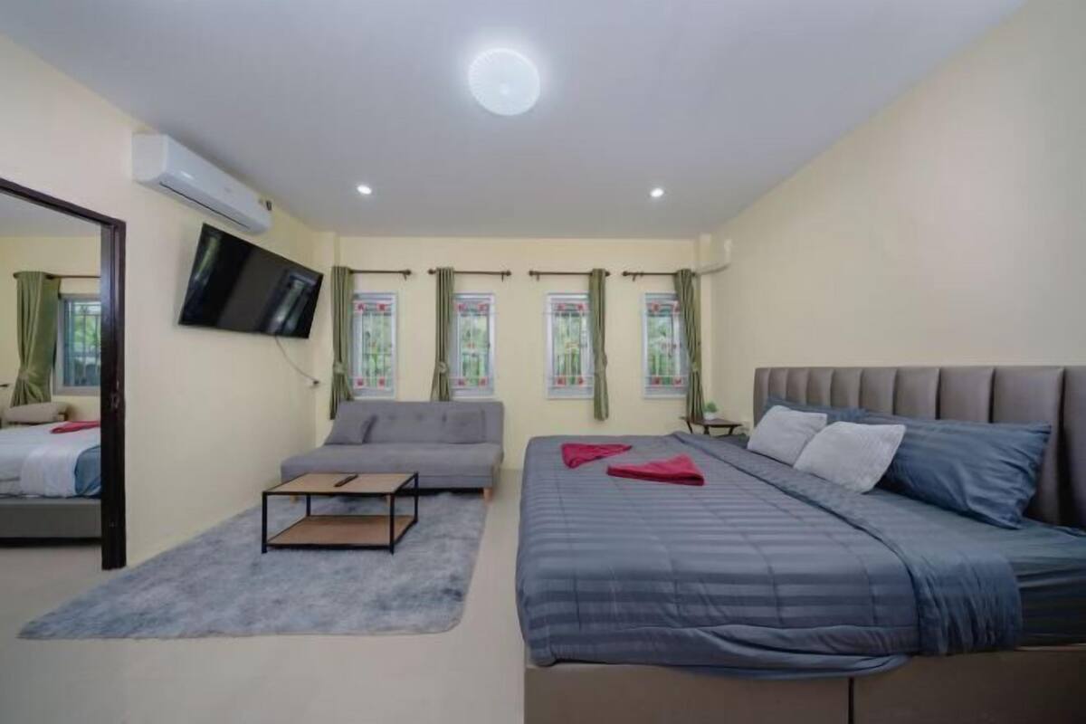 A bedroom with a bed, a sofa, a TV, and a window with curtains.