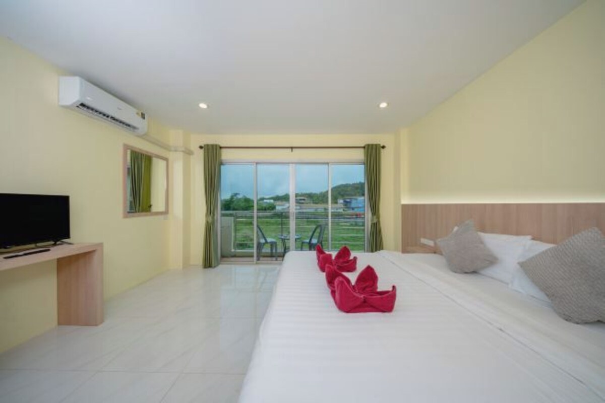 A hotel room with a bed, a TV, a balcony with a view, and an air conditioning unit.