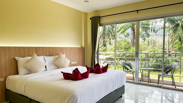 A hotel room with a large bed, a balcony with a table and chairs, and a view of greenery. - Nan's Aonang (Krabi)