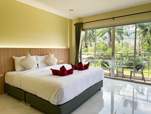 A hotel room with a large bed, a balcony with a table and chairs, and a view of greenery.