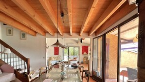 A spacious dining area with a glass table, wooden chairs, and a wooden ceiling.