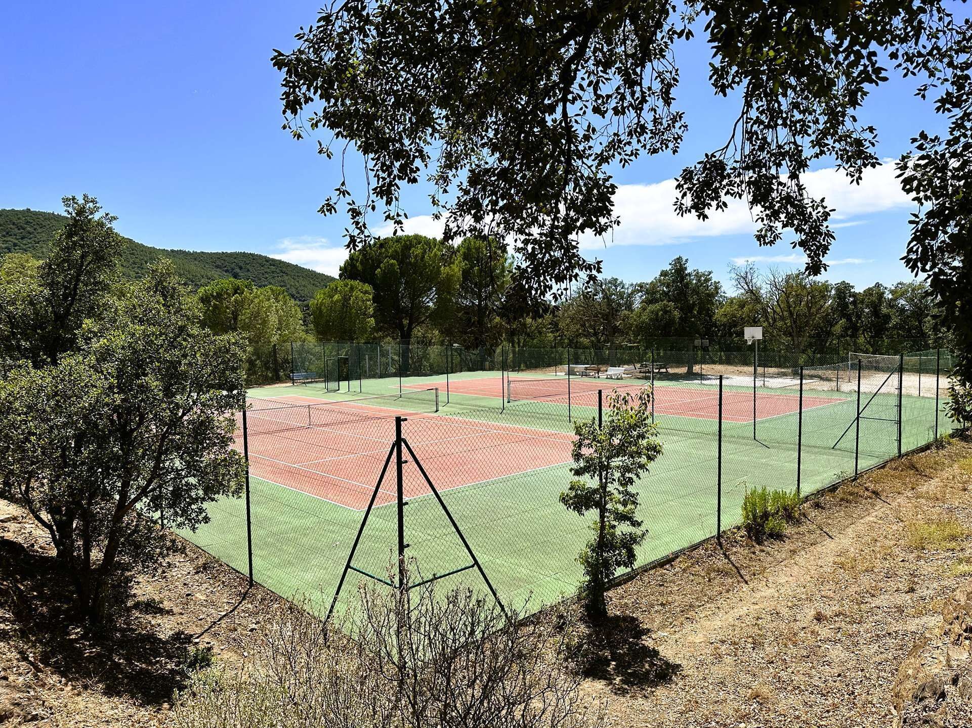 Una cancha de tenis rodeada de árboles y colinas.
