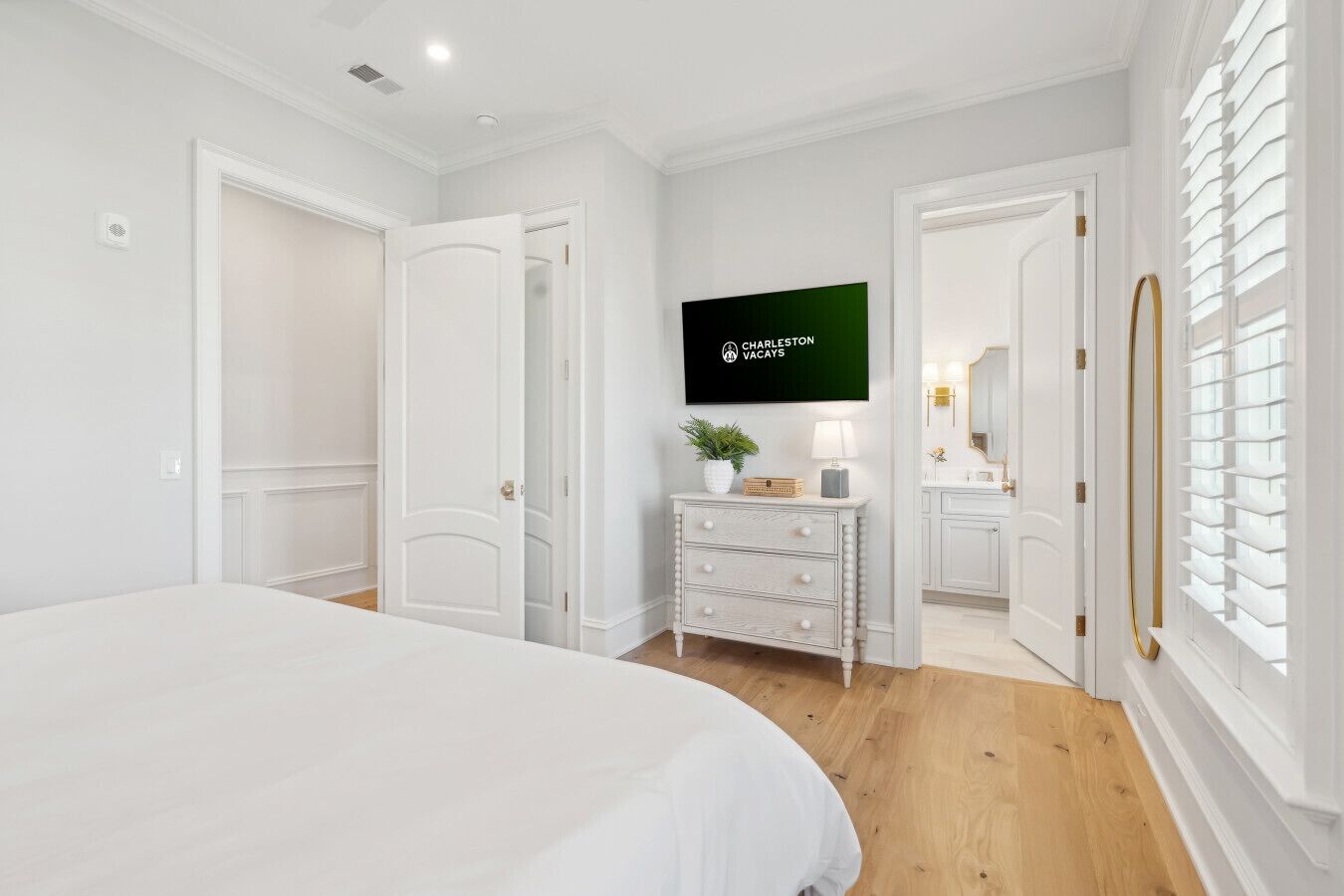A bedroom with a large bed, a dresser, a TV, and a bathroom visible through an open door.