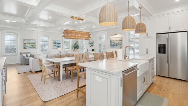 A modern kitchen with white cabinetry, a stainless steel refrigerator, and a dining area with a white table and chairs.