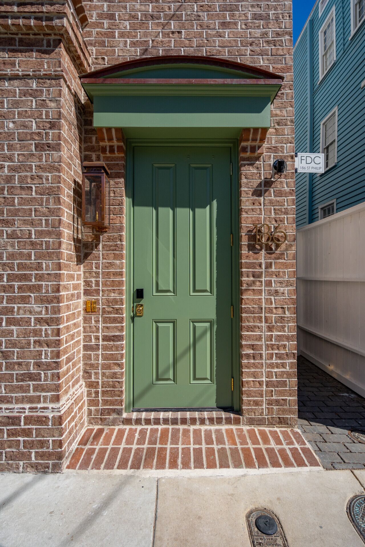 A green door with a brick facade, a small window with a lantern, and a sign reading "FDC 186 St Philip".