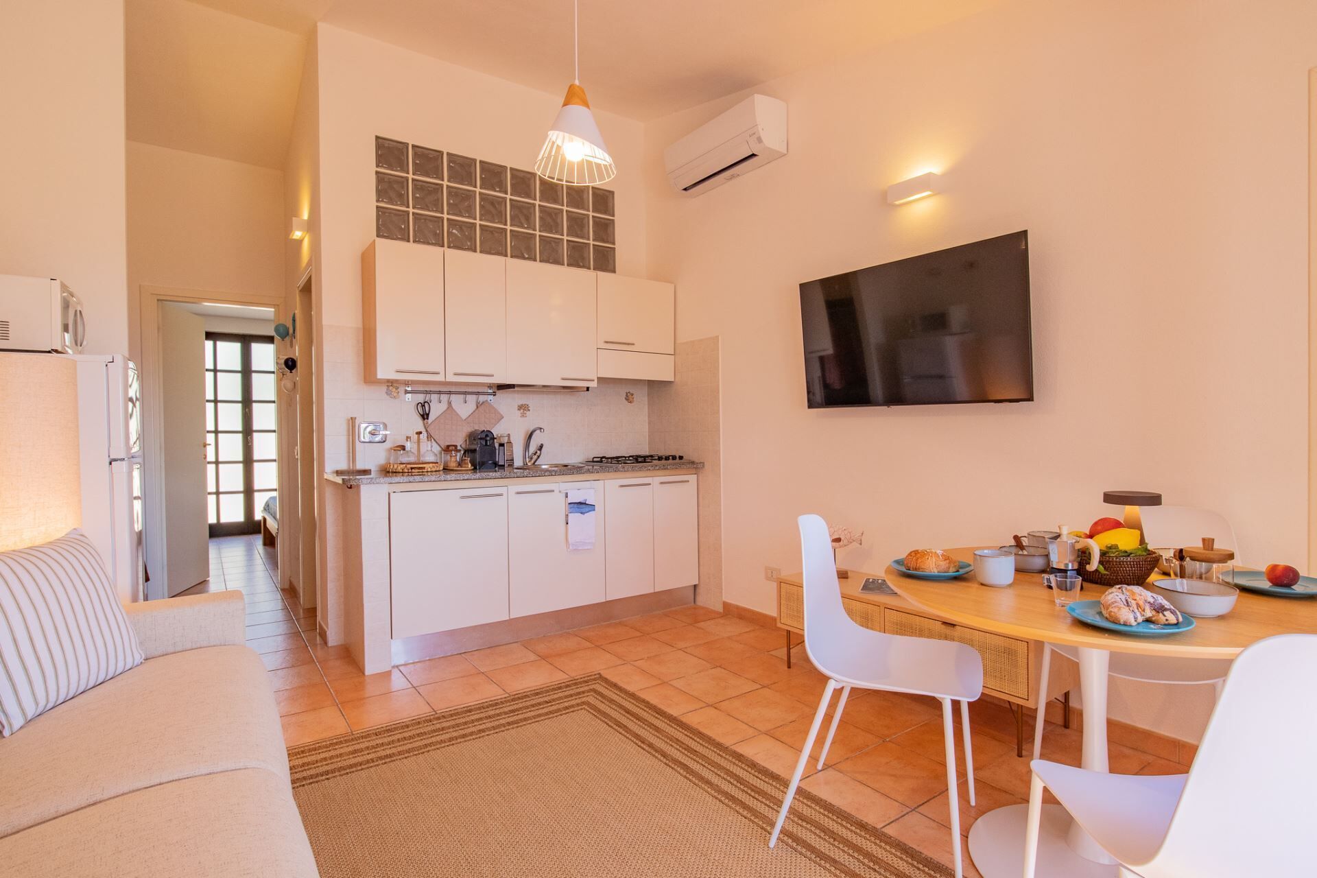 A compact kitchen with white cabinets, a dining area with a table and chairs, and a TV mounted on the wall.