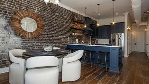 A modern kitchen with a brick wall, a round mirror, a dining table with chairs, and a blue island with stools.