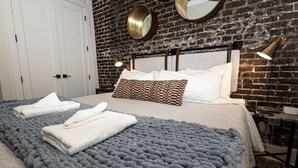 A hotel room with a large bed, a brick wall, two round mirrors, and a bedside table with a lamp.
