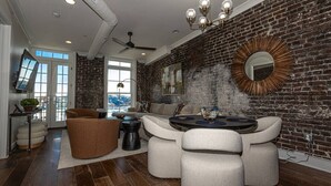 A modern living room with a brick wall, a round dining table, and a ceiling fan.