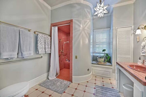 A bathroom with a shower, a toilet, a sink, and a window with blinds.