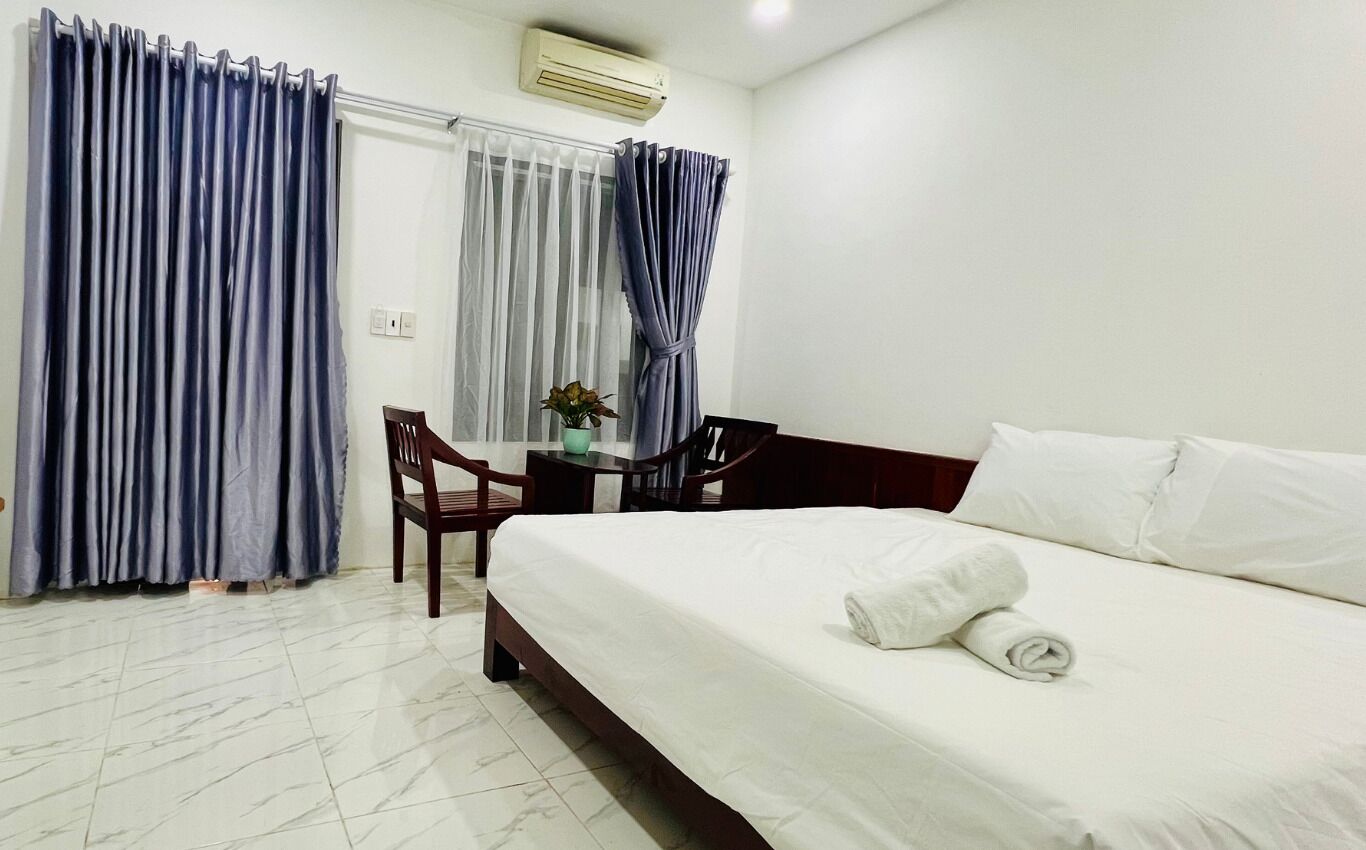 A hotel room with a bed, a desk, a chair, and a window with curtains.
