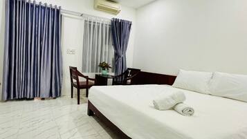 A hotel room with a bed, a desk, a chair, and a window with curtains.