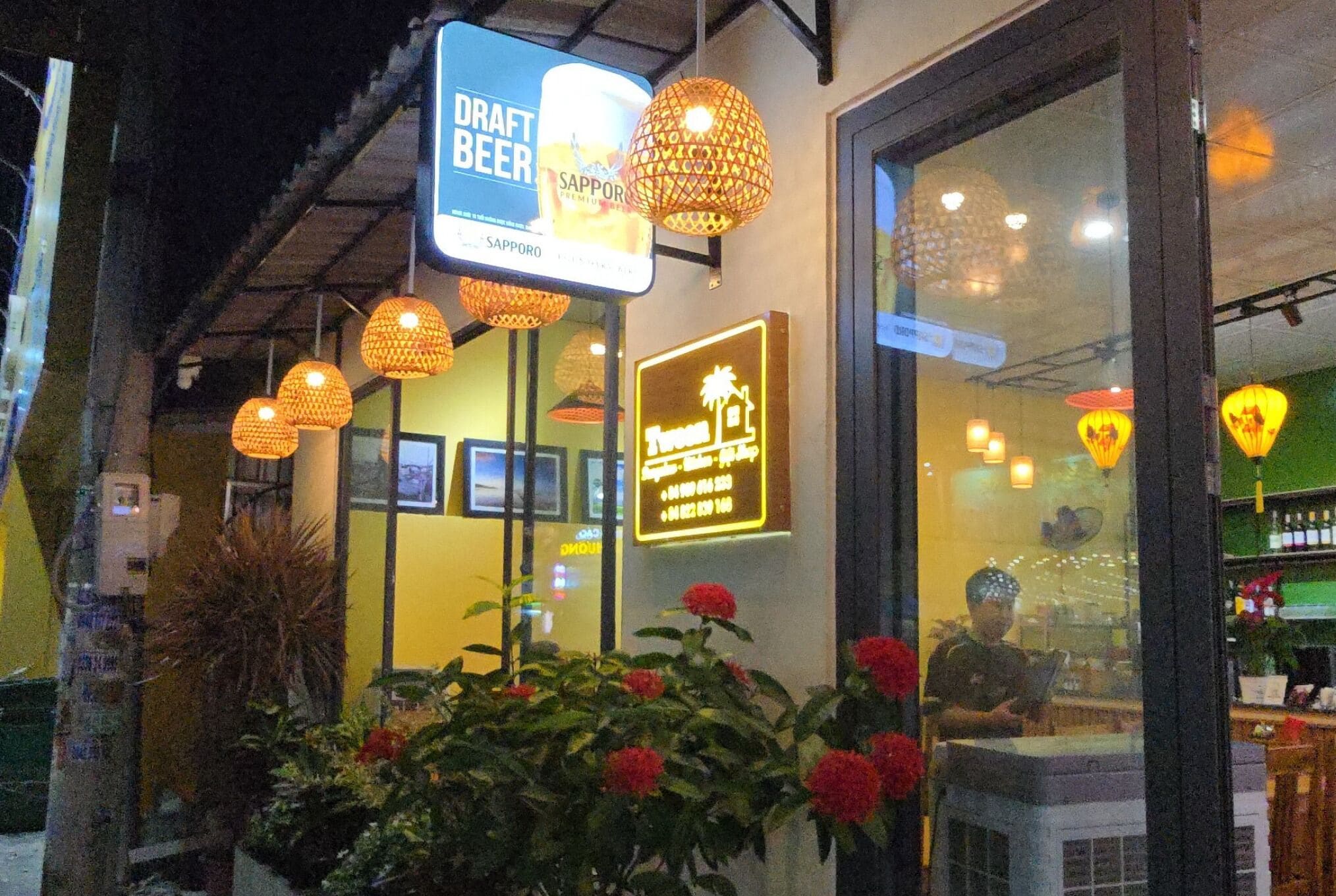 A restaurant with a sign for 'Draft Beer' and 'Sapporo'. There are hanging lights and a window with reflections.