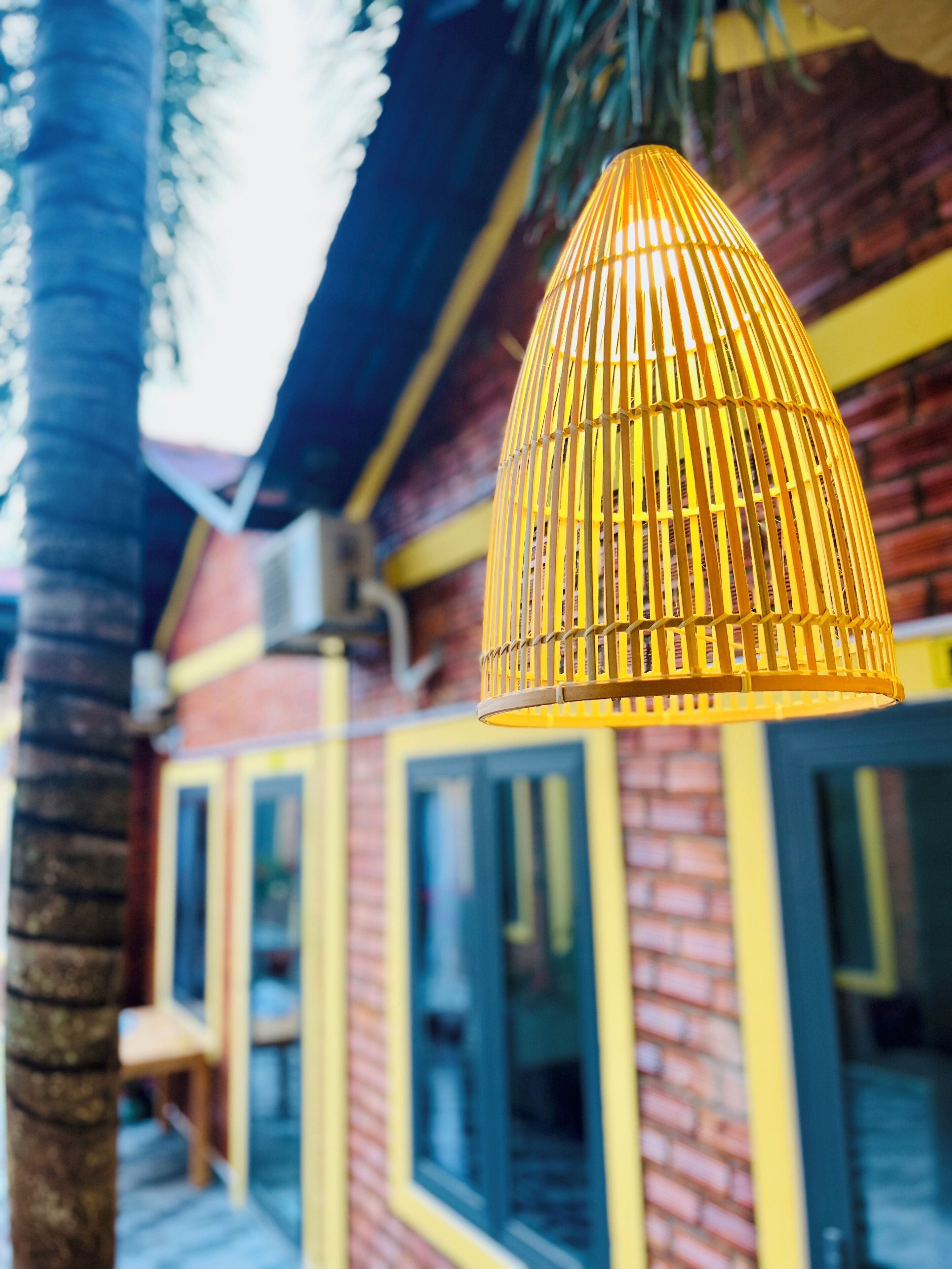 Un luminaire suspendu de couleur jaune dans une pièce dotée d’un mur en briques et de grandes fenêtres.