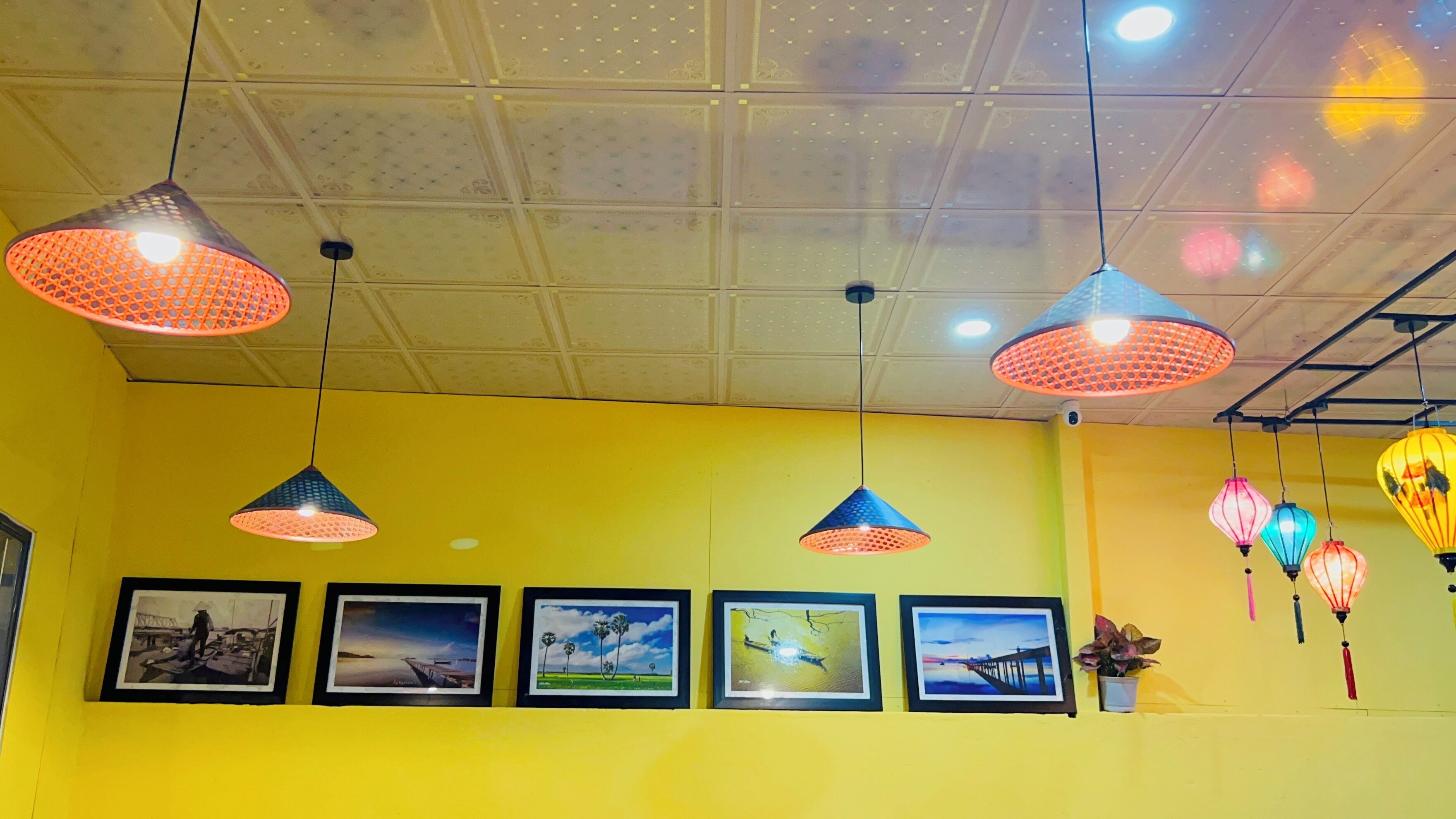 A room with yellow walls, multiple hanging pendant lights, and framed pictures on the wall.
