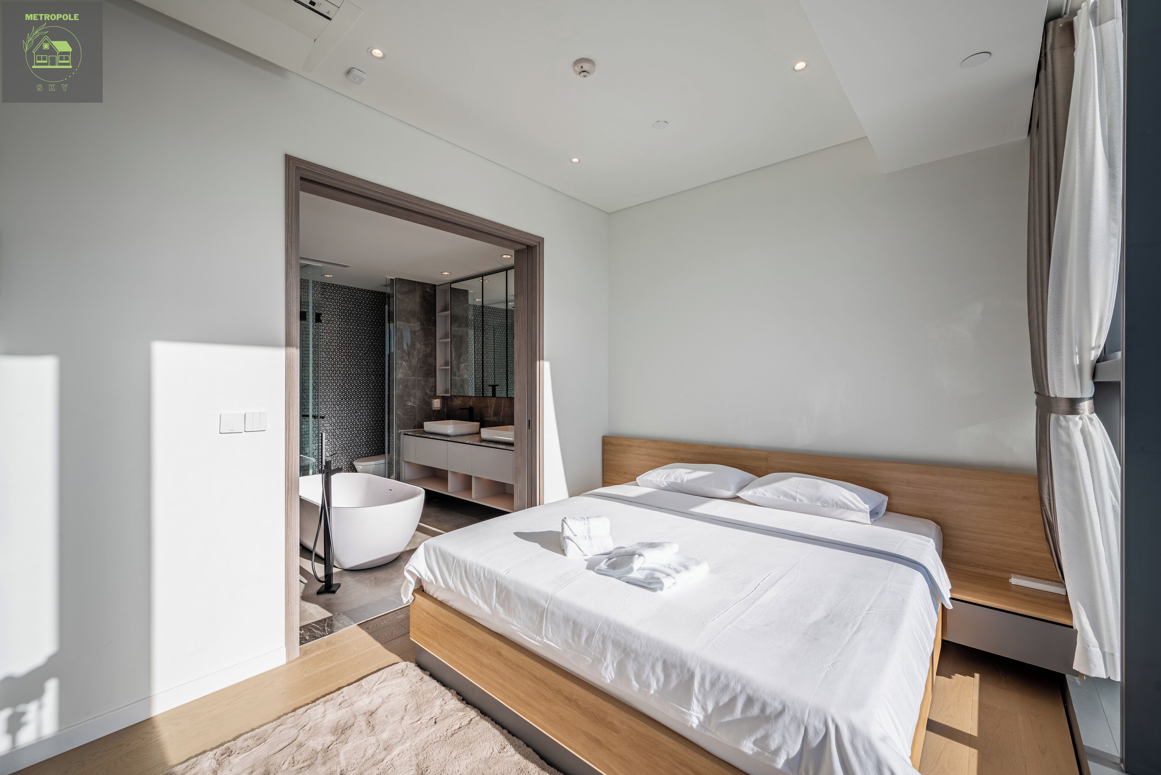 Una habitación de hotel moderna con una cama grande, un baño con bañera y vistas a la ciudad.