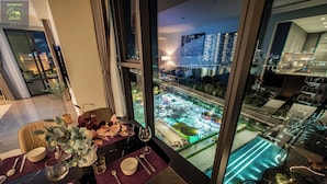 Comedor con una mesa para dos, vistas a la ciudad a través de amplios ventanales y una zona de piscina visible en el exterior.