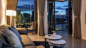 Una habitación de hotel moderna con vistas a la ciudad, un sofá, una silla, una mesita y una lámpara.