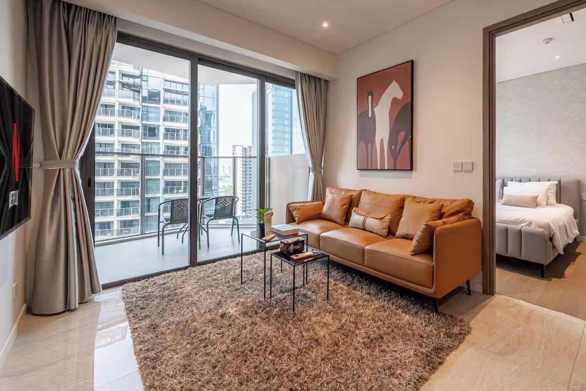 Una sala de estar moderna con un ventanal grande, un sofá, una mesa de centro y vista a un edificio de gran altura.