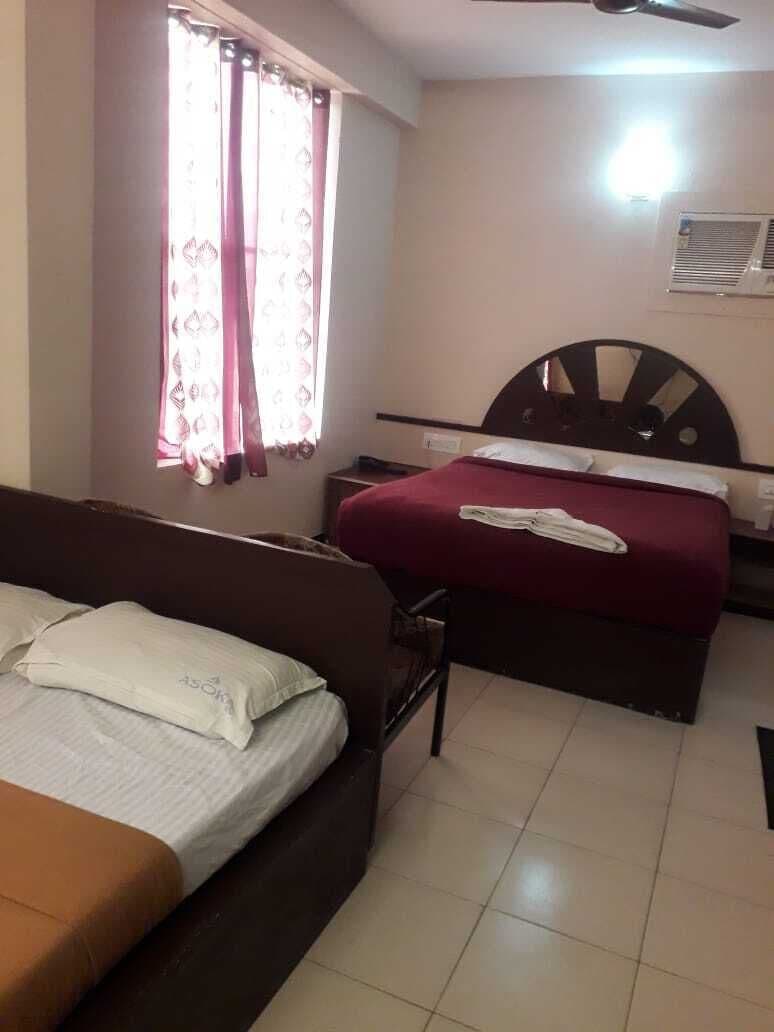 Habitación de hotel con dos camas, ventilador de techo y ventana con cortinas.