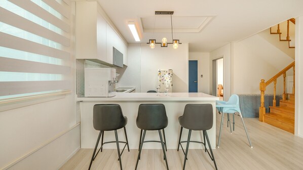 A modern kitchen with a white countertop, three black bar stools, and a decorative light fixture. - Sokcho Biroso Private Cottage (Sokcho)